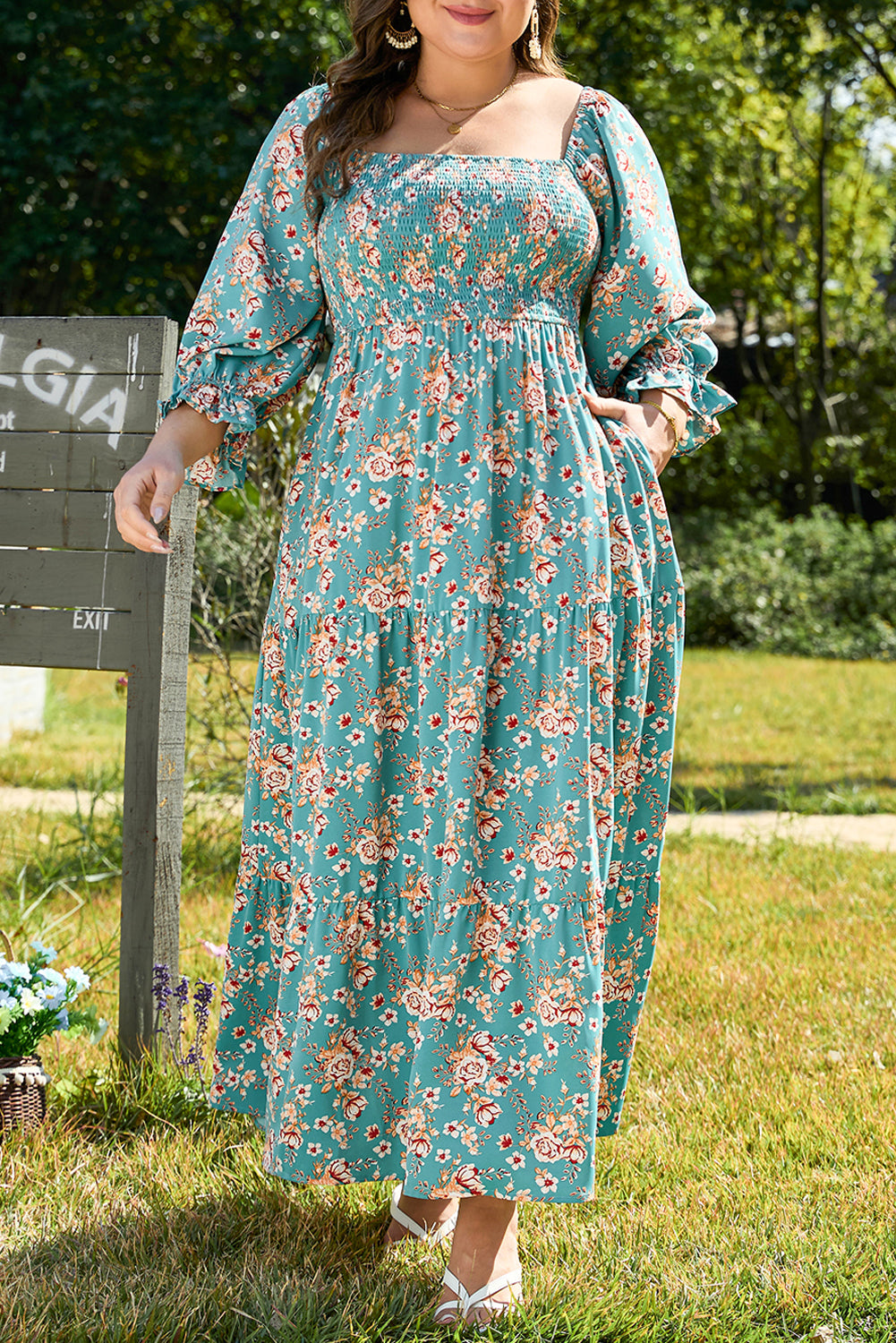 Woman wearing a floral dress standing outdoors with greenery in the background
