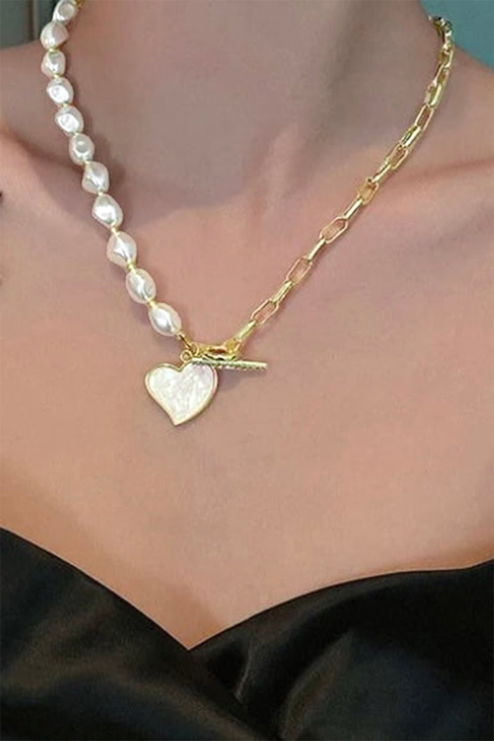 Necklace with heart-shaped pendant and pearl beads on a person wearing a black top.